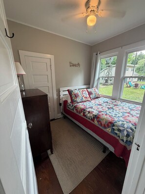 Une chambre à coucher avec un lit, une commode, une porte et une fenêtre.