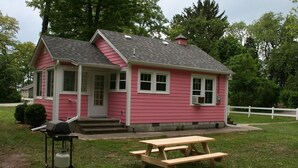 Et pink hus med veranda, picnicbord og grill i haven.