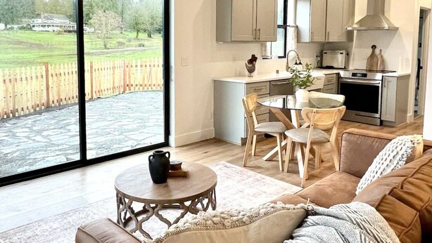 A modern kitchen with a dining area, large windows, and a cozy living room with a leather sofa and a fireplace.