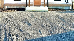 A single-story house with a front porch, a wooden door, and two windows on the side.