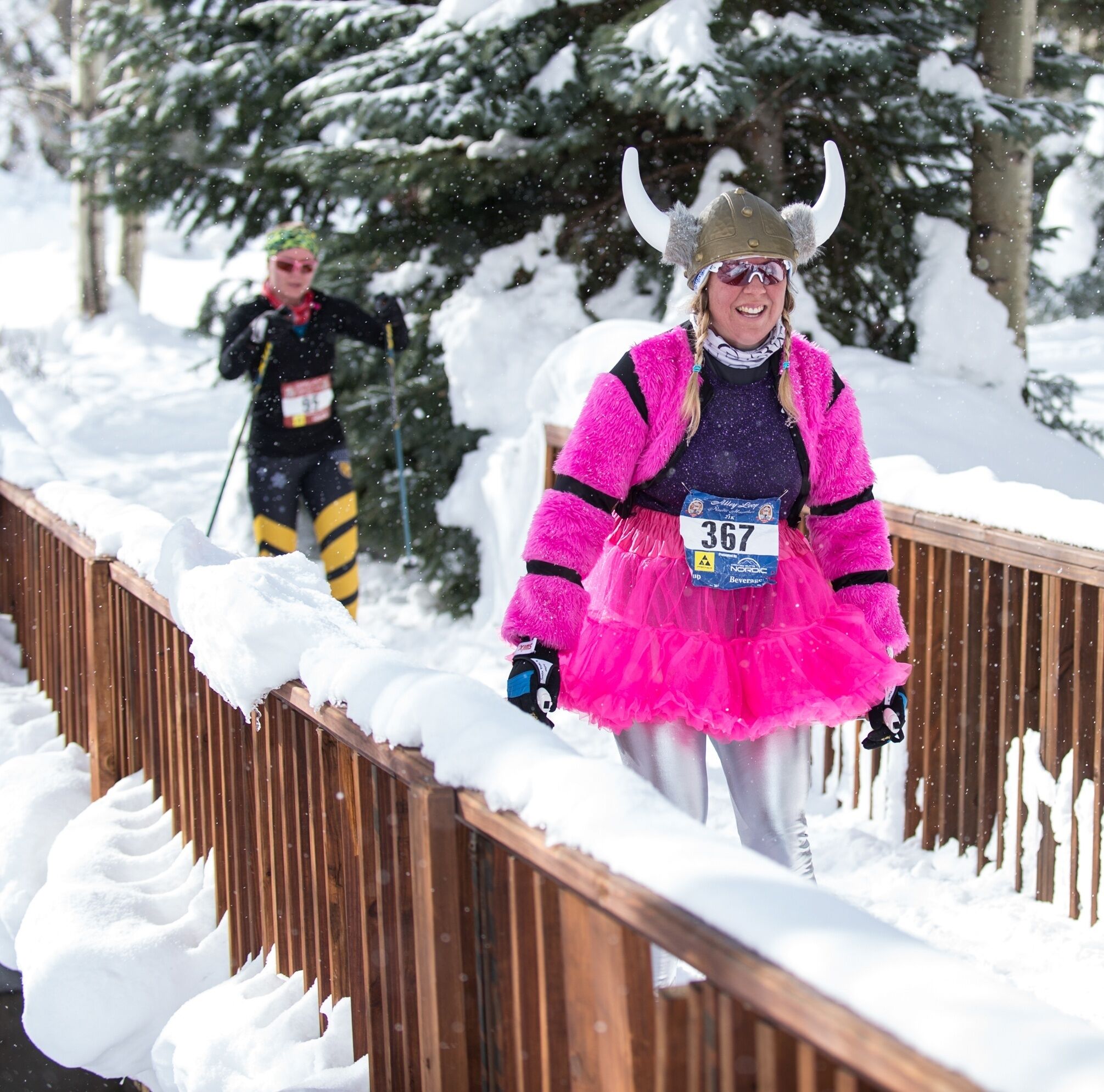 A snow-covered wooden bridge with a person in a pink costume and a Viking helmet walking on it.