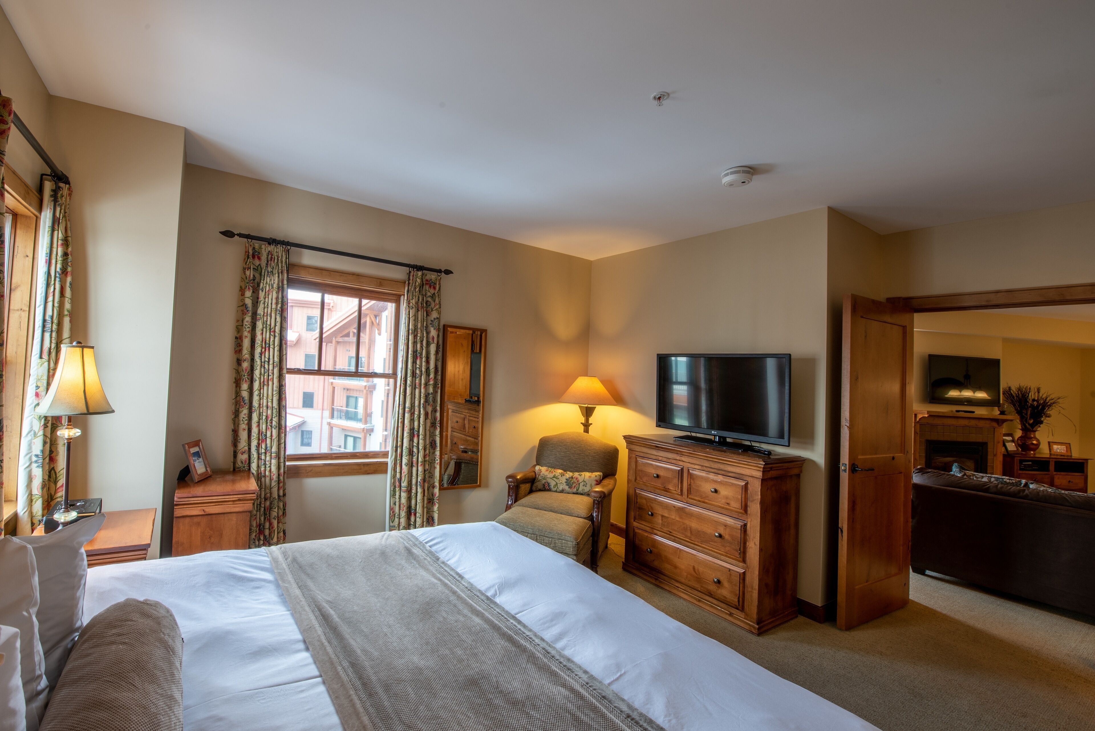 Habitación de hotel con una cama grande, televisión, cómoda de madera y ventana con cortinas.