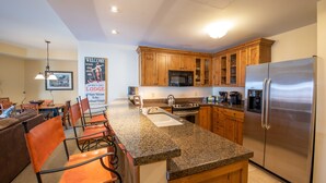 A kitchen with granite countertops, wooden cabinets, stainless steel appliances, and a dining area with chairs and a table. - Comfortable 1 Bedroom Slopeside Condo - No Cleaning Fee! by RedAwning (Crested Butte)