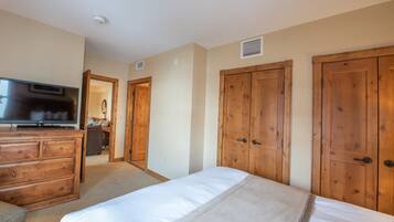 A bedroom with a bed, wooden wardrobe, a TV on a dresser, and a door leading to another room.