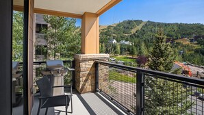 A balcony with a grill, chairs, and a view of a hilly landscape. - Edgemont 2508 Luxury On Mountain Condo With Ski-In/Ski-Out Access! (Steamboat Springs)