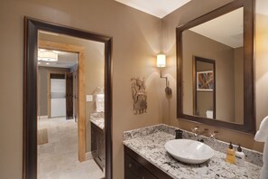 Un baño con un espejo grande, un lavabo y una tocador. Hay una toalla colgando en el lado derecho del espejo.