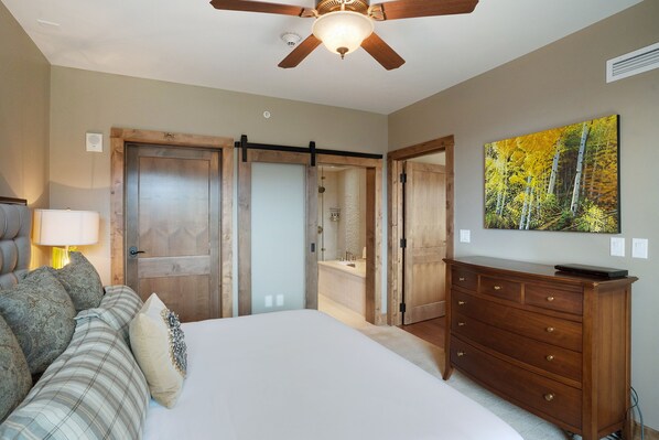 Un dormitorio con cama, cómoda, ventilador de techo y un cuadro de un bosque.