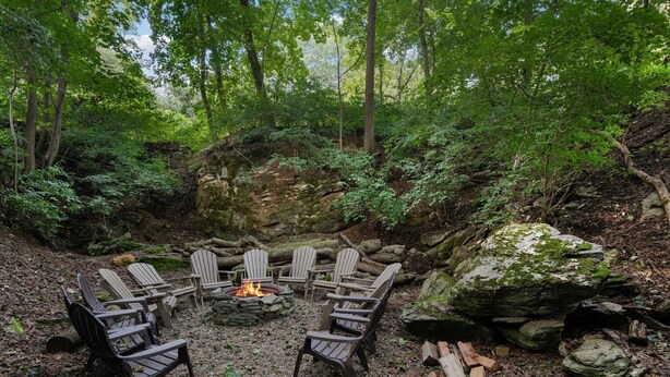 A circular seating arrangement with Adirondack chairs around a central fire pit in a forested area. - Endless Family Fun @ Private LUX Retreat Sleeps 25 (Annville)