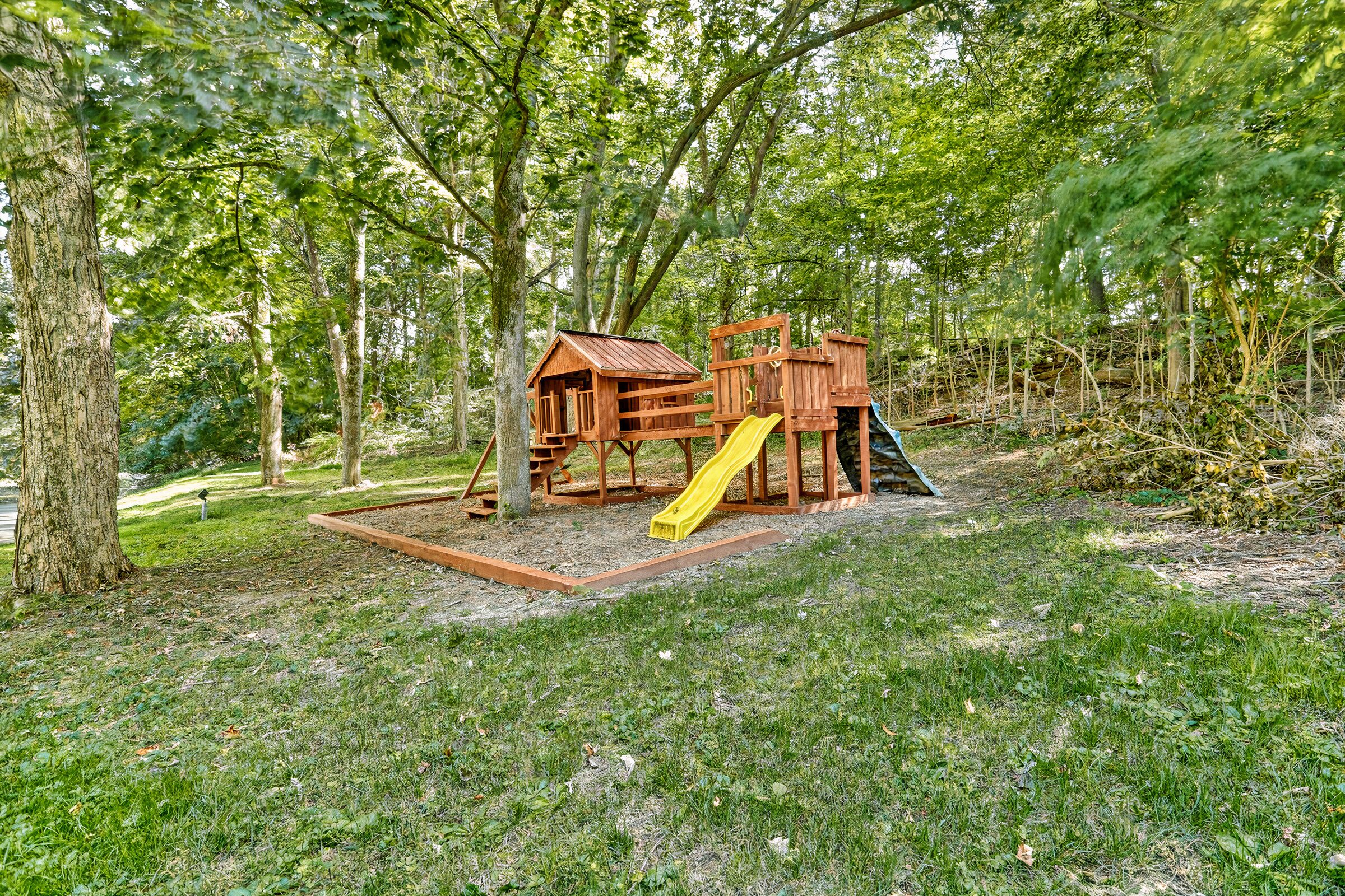Estructura de madera para juegos con un tobogán y zona de escalada, rodeada de árboles.