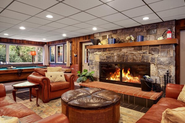 A cozy lounge area with leather sofas, a billiards table, and a stone fireplace.