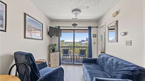 A room with a dark blue sofa, a small table, and a TV mounted on the wall. - Just steps away from the beach!  (Myrtle Beach)