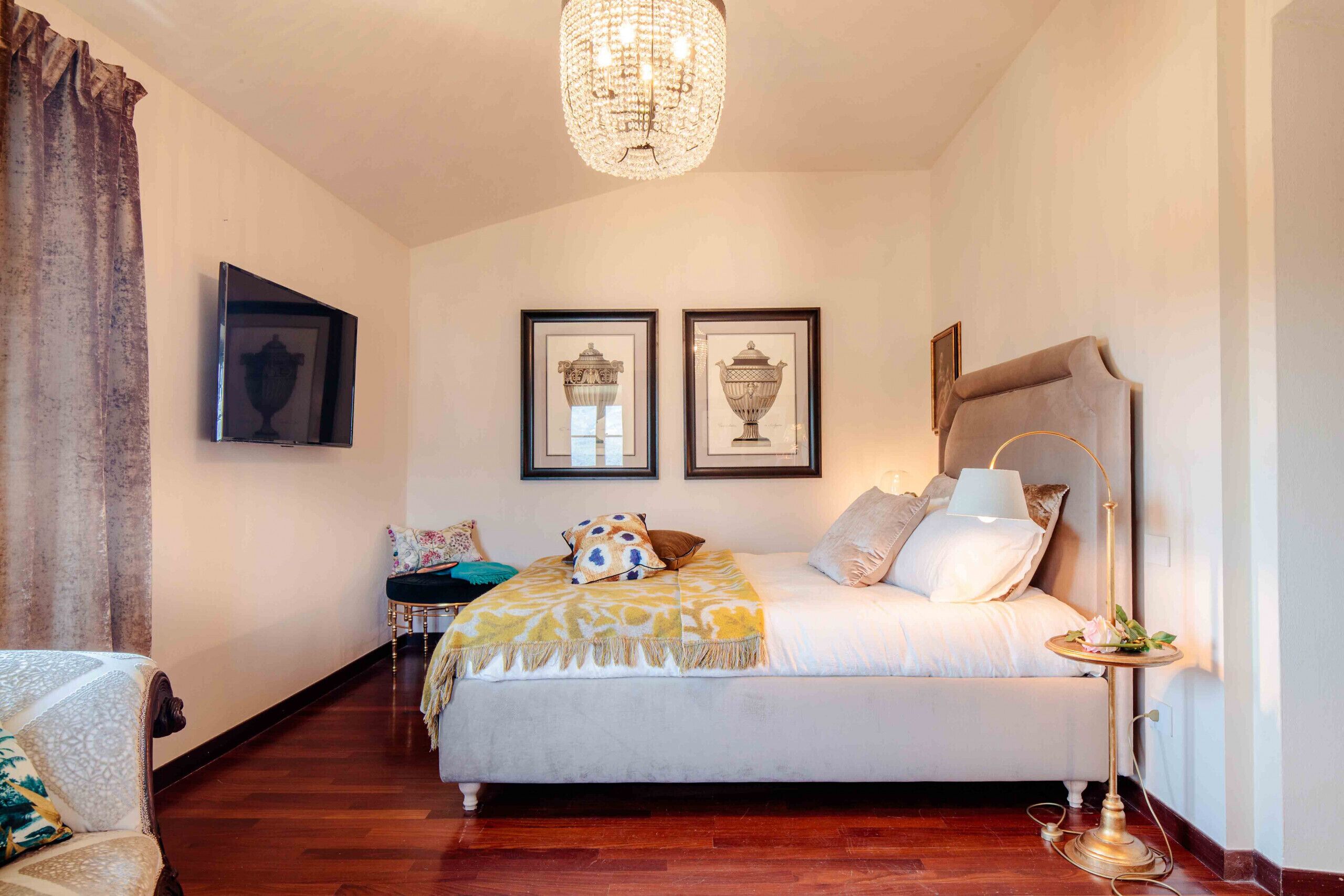 Una camera da letto con un letto, un comodino, una lampada, un lampadario e quadri appesi al muro.