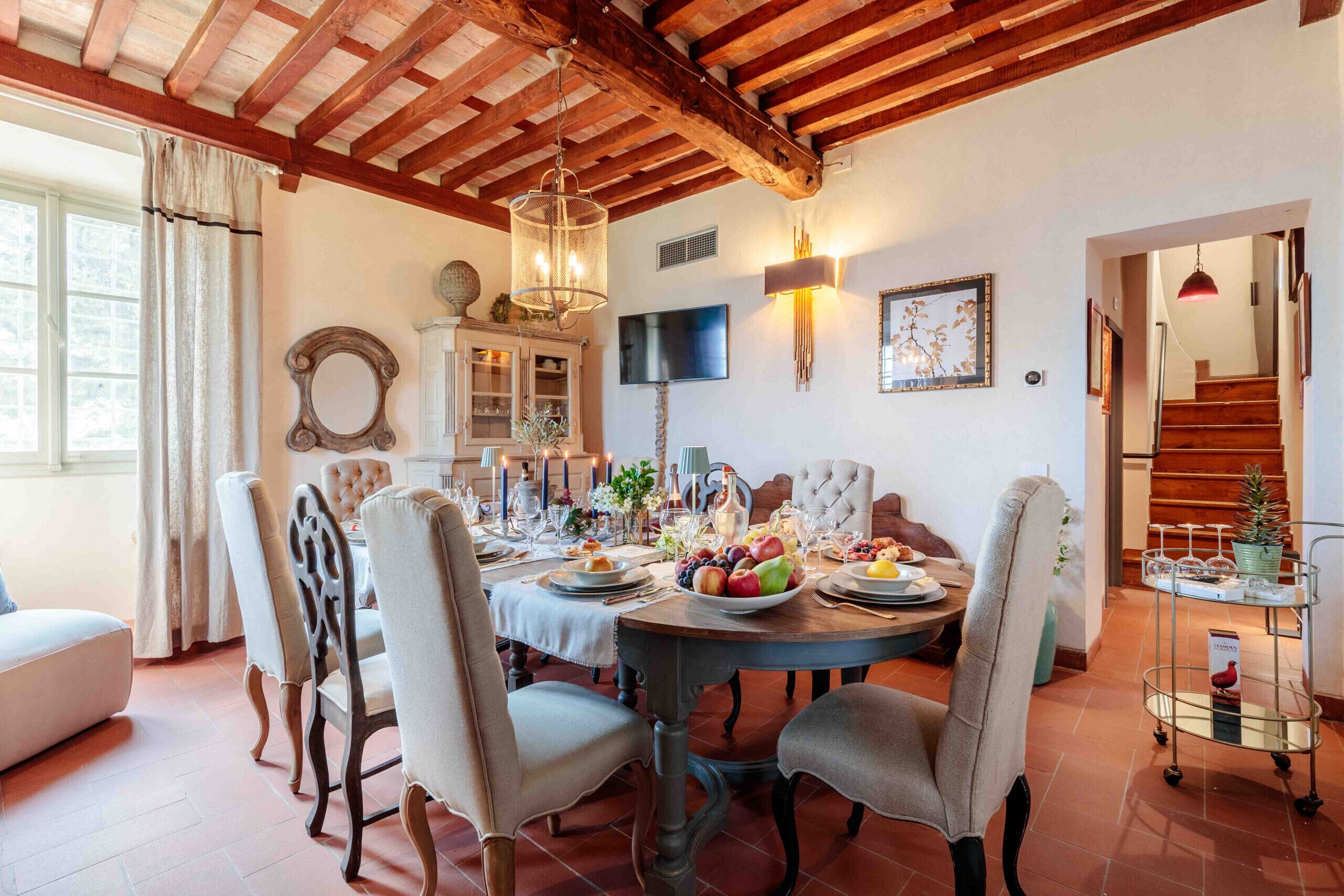 A dining room with a wooden ceiling, a round table set for six, and a TV mounted on the wall.