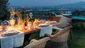 Un'area pranzo all'aperto con un tavolo imbandito per due persone, circondato da sedie in vimini, con vista sullo skyline urbano.
