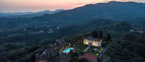 A villa with a swimming pool surrounded by lush greenery and hills in the background.