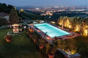 A rectangular swimming pool with a view of a cityscape at dusk. - VILLA IL CASTELLO: Vibrant Sanctuary of Enchanting Colours. 6 Bedrooms, Private Pool (Lucca)