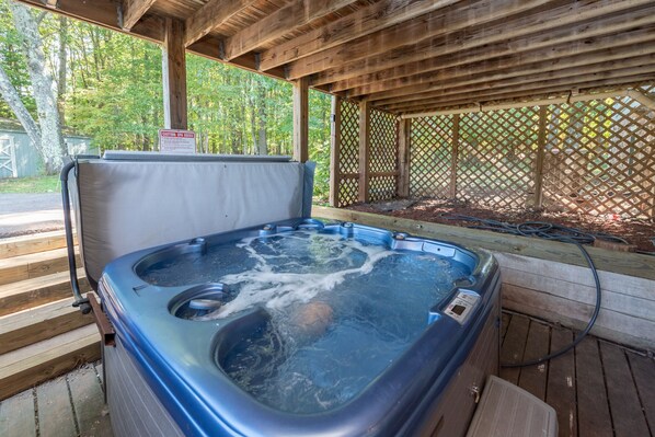 Un bain à remous installé sous une pergola en bois, avec une terrasse en bois et un panneau d’avertissement indiquant que l’eau est chaude.