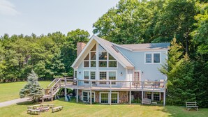 A large, light blue house with a wrap-around porch and a stone chimney. - Cozy Dog Friendly Blue Home Near Lake w/ Huge Yard (Swanton)