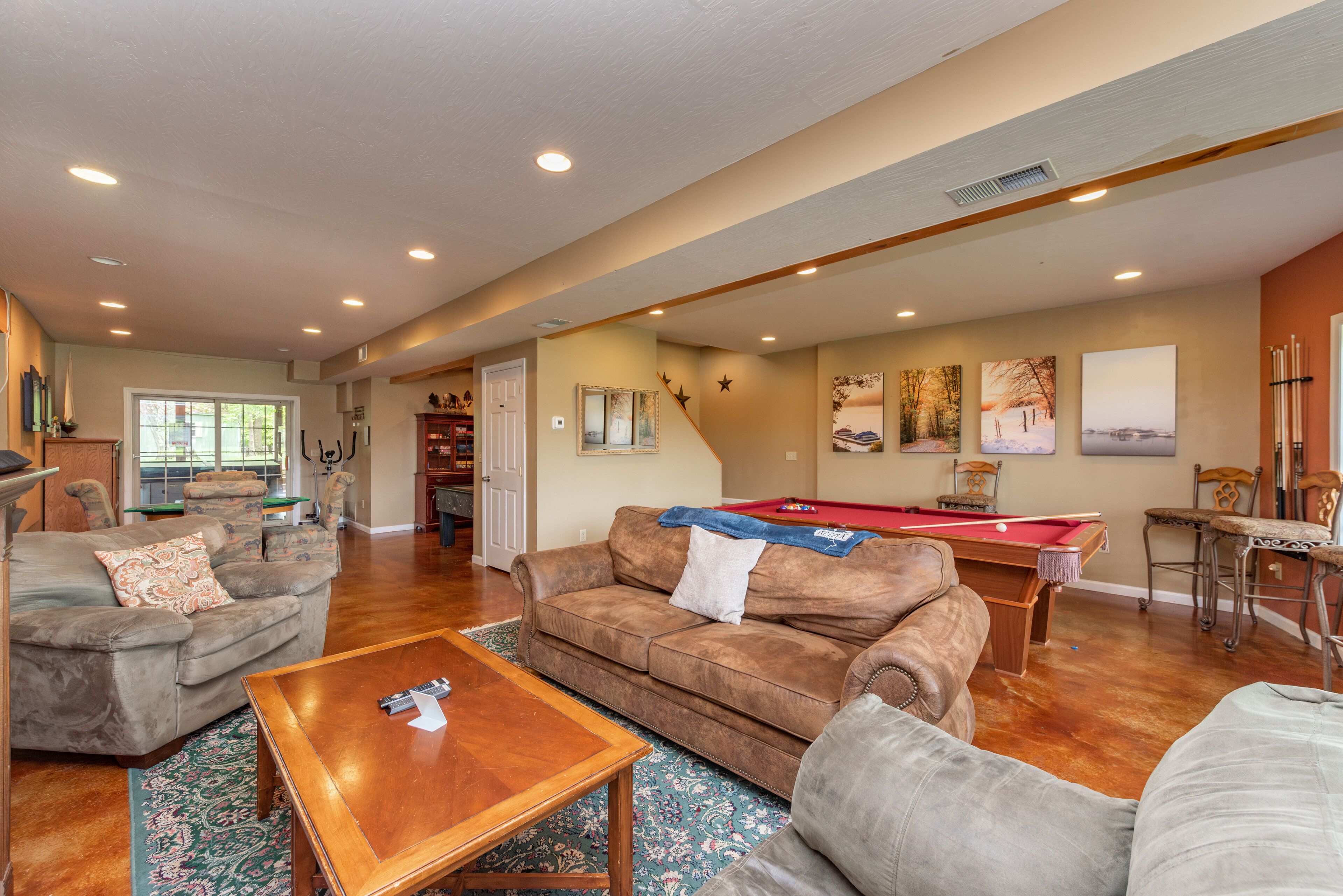 A spacious living room with a pool table, comfortable seating, and a large window providing natural light.