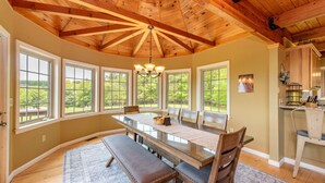 A dining area with a large table, benches, and a view of the outdoors through large windows. - Cozy Dog Friendly Blue Home Near Lake w/ Huge Yard (Swanton)