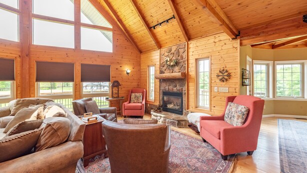 A log cabin interior with a fireplace, large windows, and a cozy seating area. - Cozy Dog Friendly Blue Home Near Lake w/ Huge Yard (Swanton)