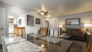 A modern living room with a glass-top dining table, a brown leather sofa, and a ceiling fan. - Spectacular Condo In Downtown Whitefish, Close To Glacier Park, Skiing And Golf (Whitefish)