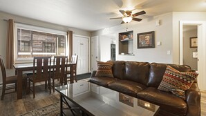 A living room with a leather sofa, a glass coffee table, a dining table with chairs, and a ceiling fan. - Spectacular Condo In Downtown Whitefish, Close To Glacier Park, Skiing And Golf (Whitefish)