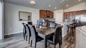 Una cocina moderna con armarios de madera oscura, un refrigerador de acero inoxidable y una zona de comedor con una mesa de madera oscura y sillas de cuero.