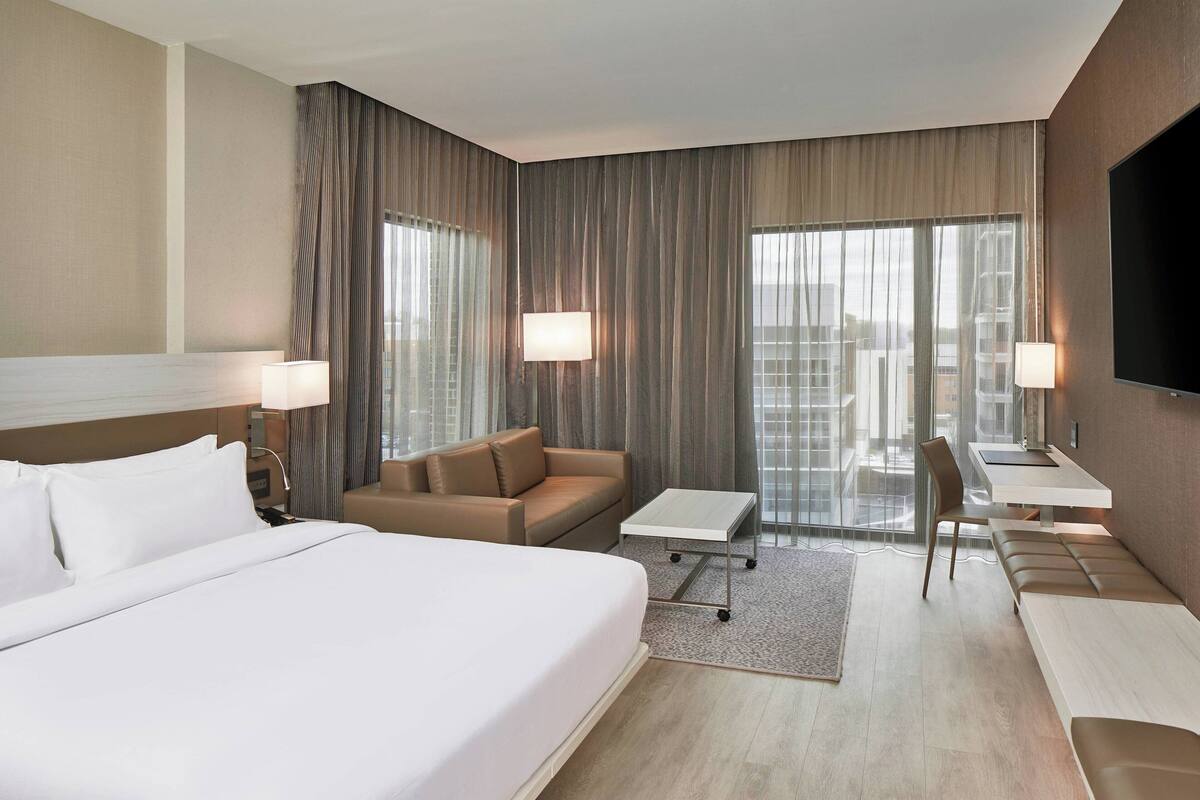 Une chambre d’hôtel moderne avec un grand lit, un canapé, une petite table et un téléviseur.