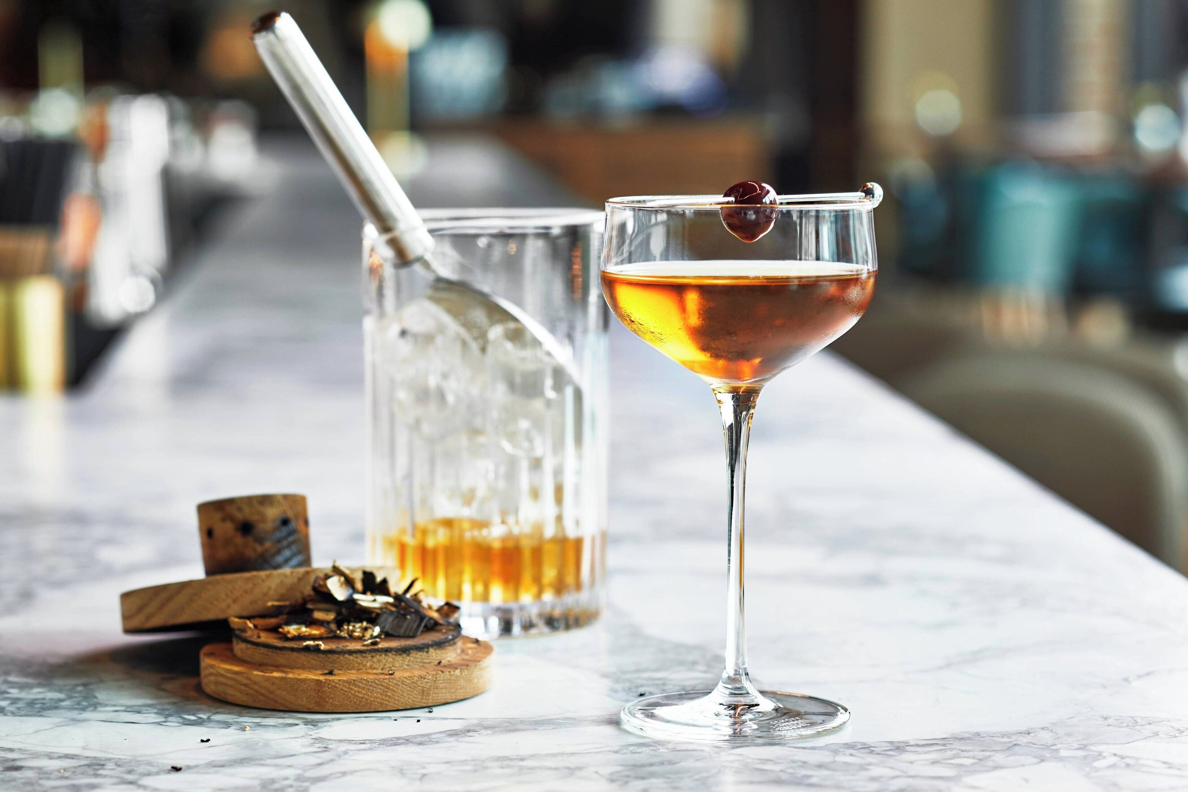 Un bar con una copa de cóctel, un vaso de whiskey y un posavasos de madera con un corcho.