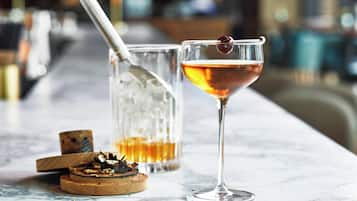 Un bar con una copa de cóctel, un vaso de whiskey y un posavasos de madera con un corcho.
