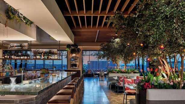 A modern bar area with a long counter, seating, and a view of the cityscape.
