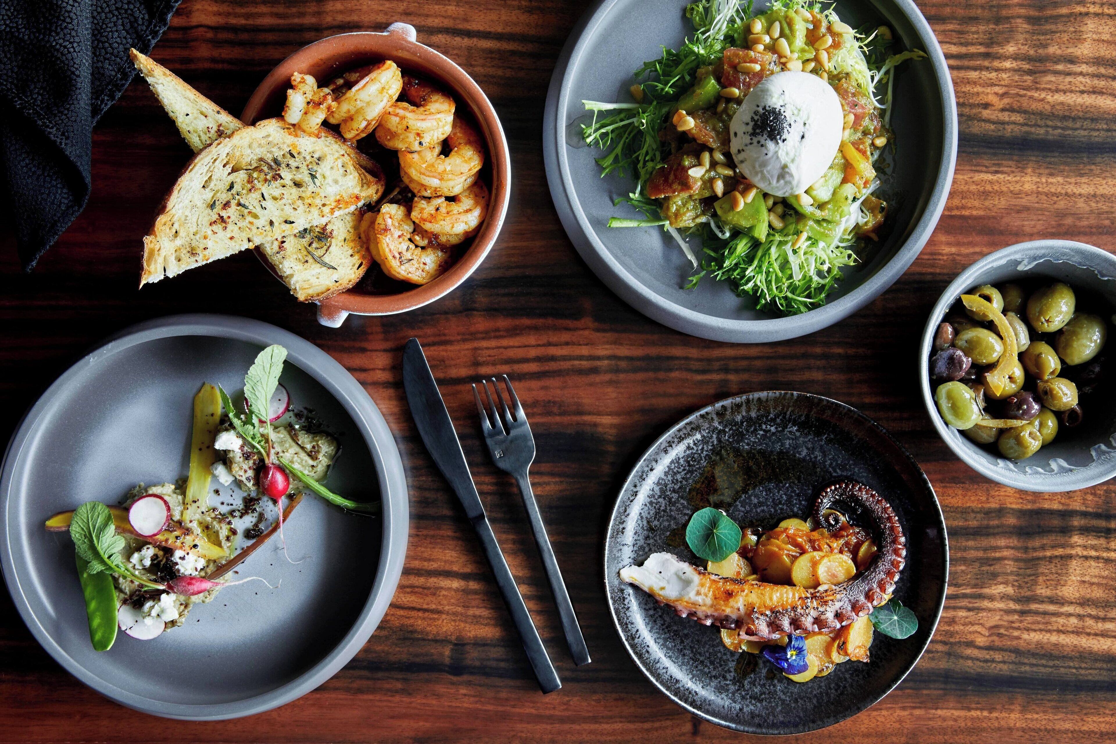 A table with various dishes, including seafood, salads, and a bowl of olives.