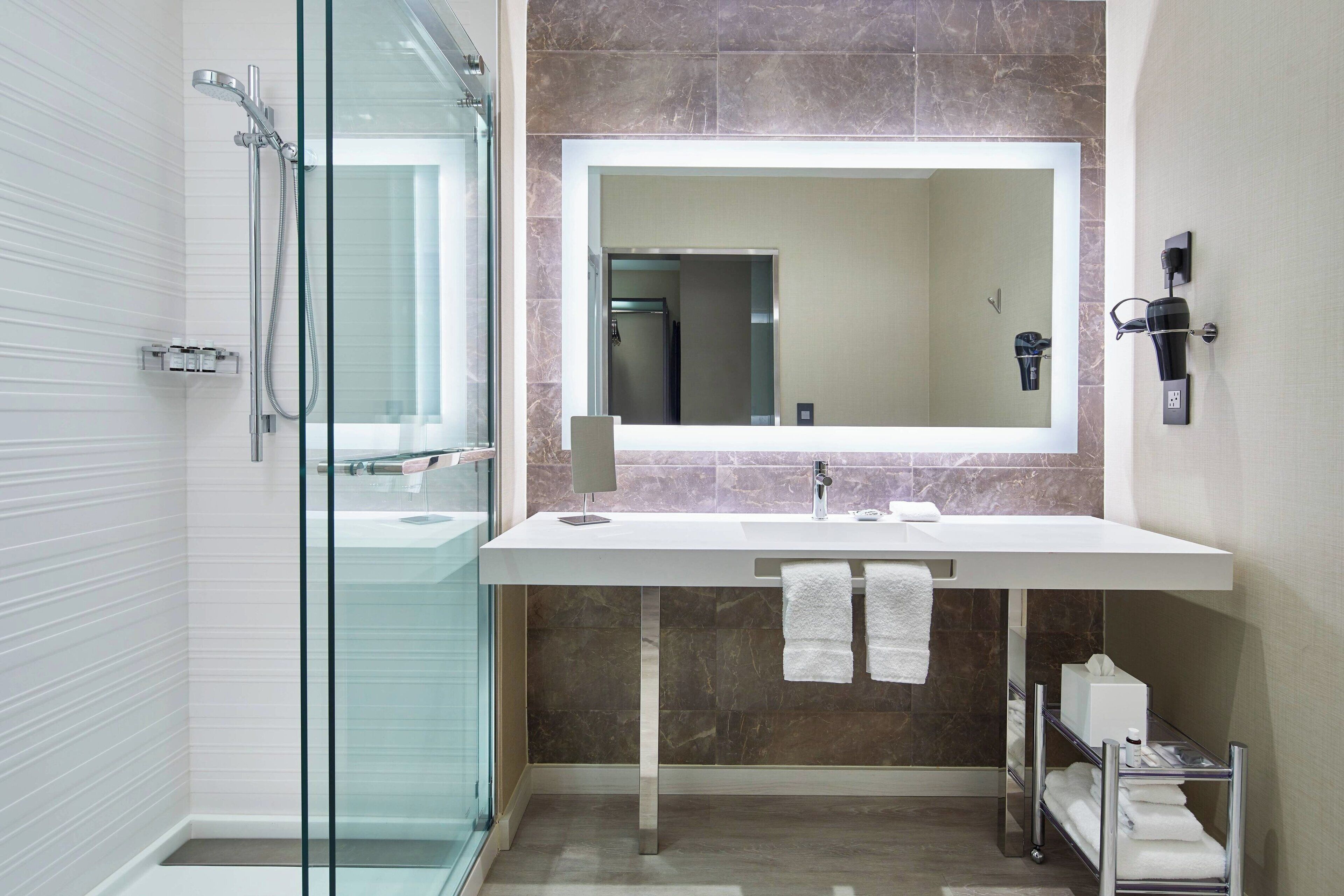 Un baño moderno con cabina de ducha de vidrio, un espejo grande y un lavamanos blanco.