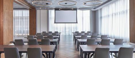 A conference room with a large screen, multiple tables, and chairs arranged for meetings.
