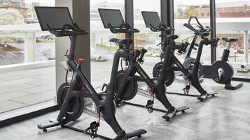 Trois vélos d’appartement, équipés d’écrans, dans un espace intérieur moderne doté de grandes fenêtres.