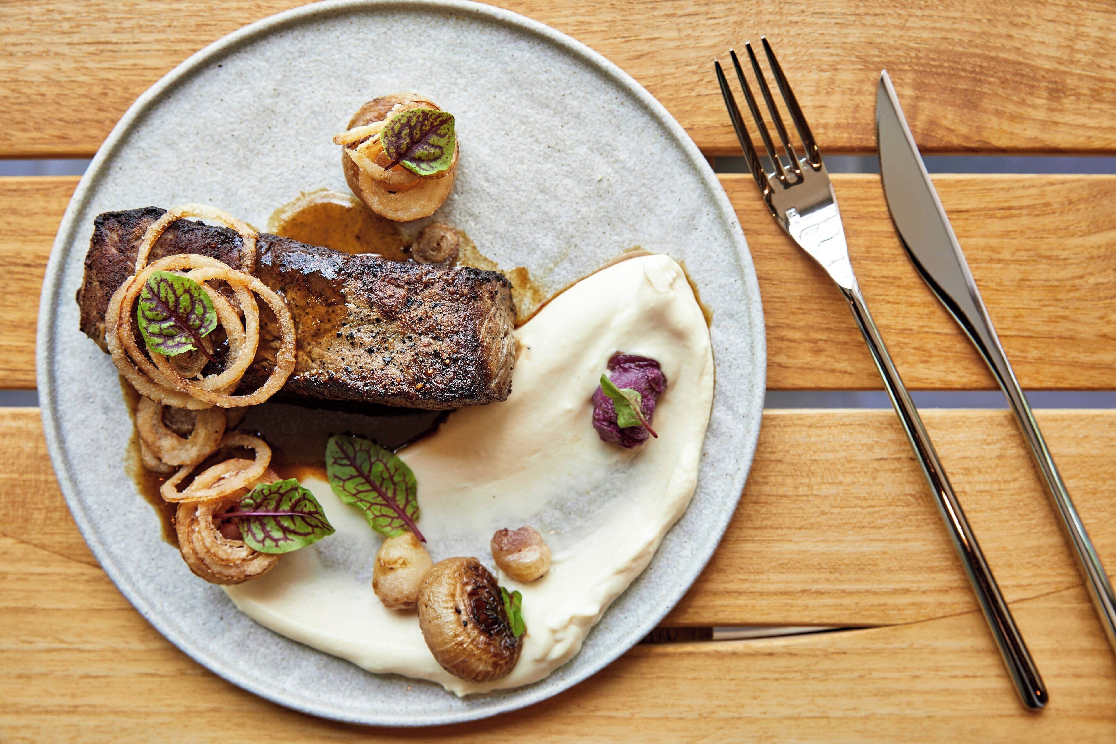 A plate of food with a steak, mushrooms, and onion rings.