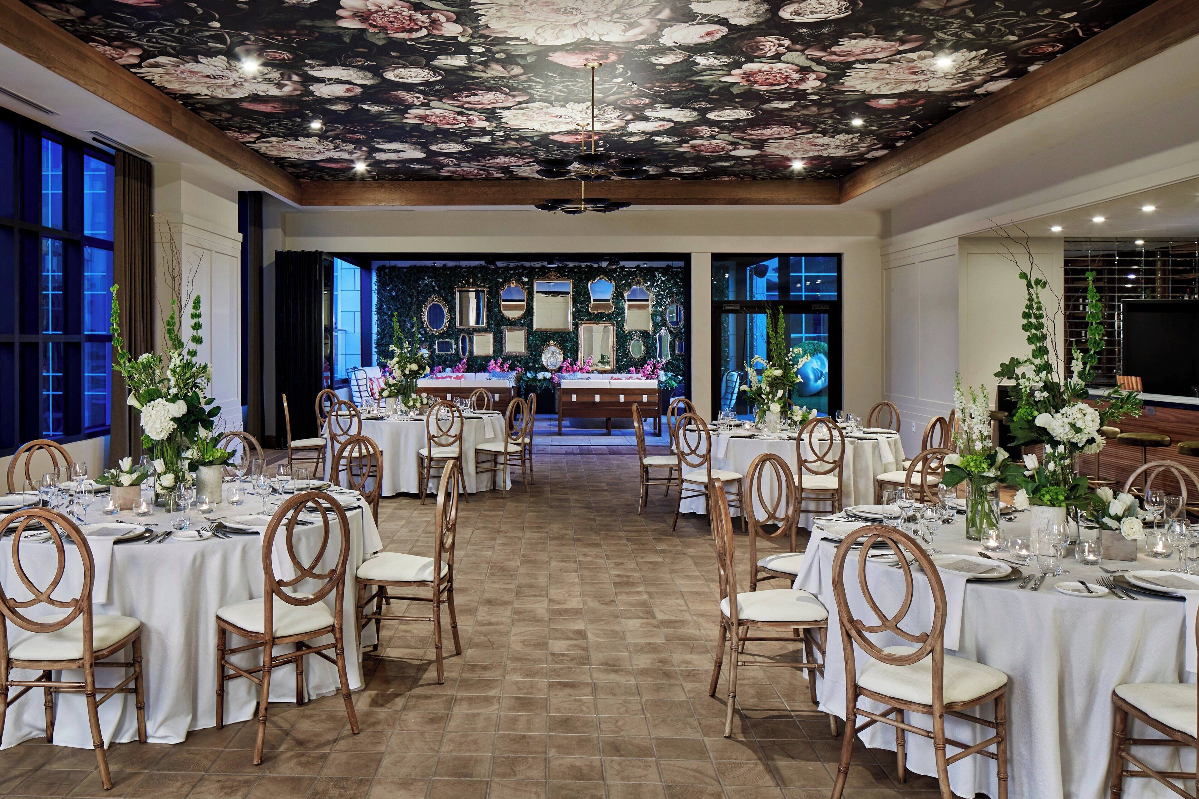 A banquet hall with round tables, white tablecloths, and wooden chairs.