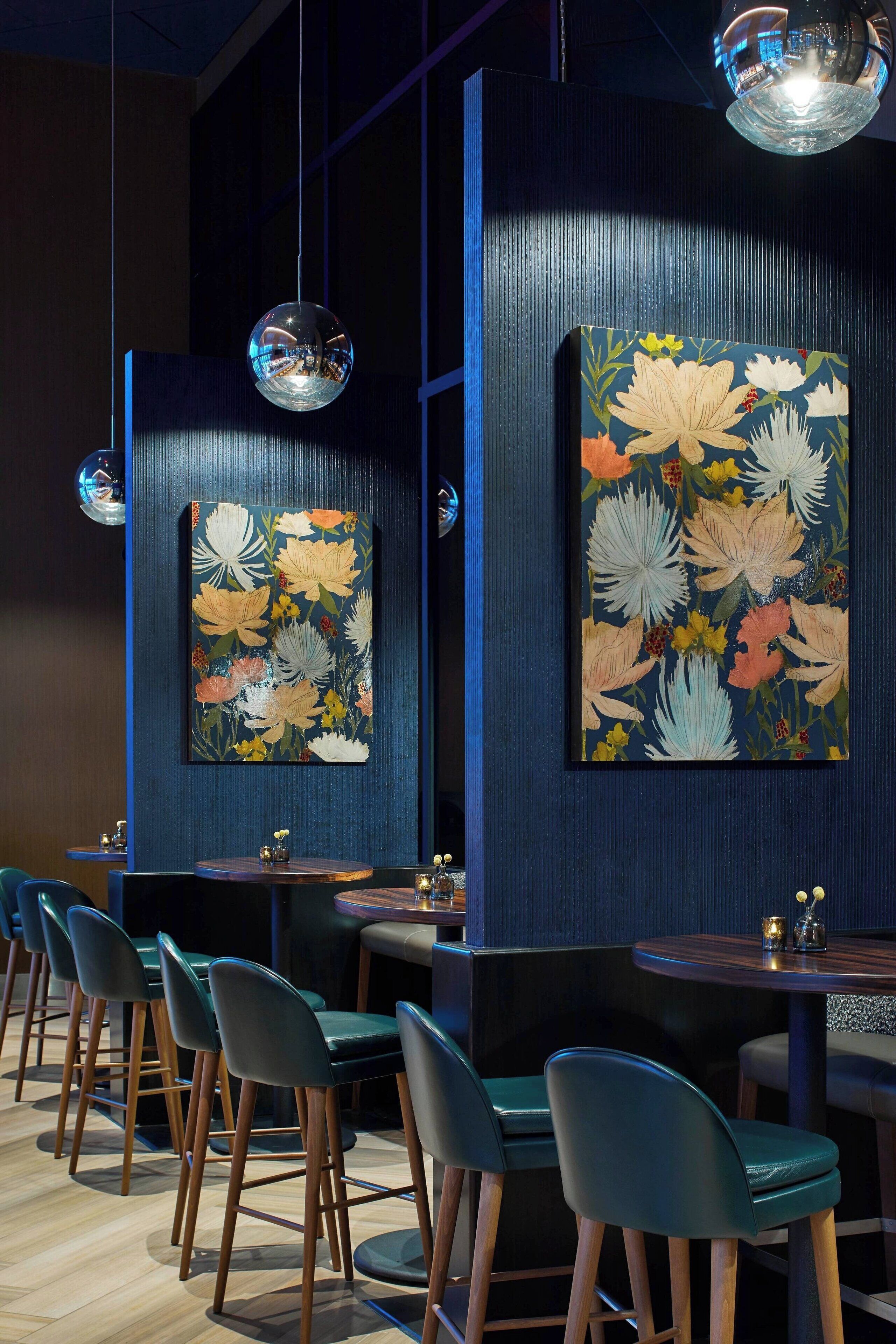 Een restaurantinterieur met houten stoelen, tafels en twee grote bloemschilderingen aan de muren.