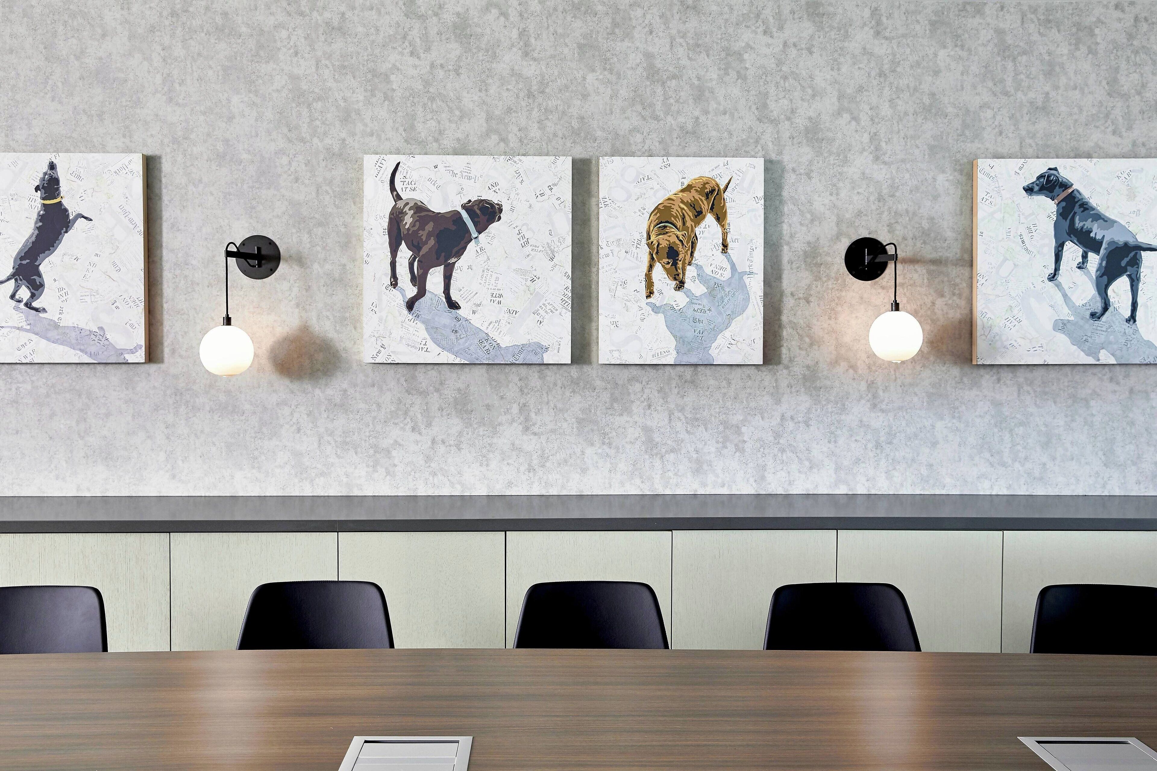 A conference room with a long table, four wall-mounted artworks of dogs, and two wall-mounted lights.