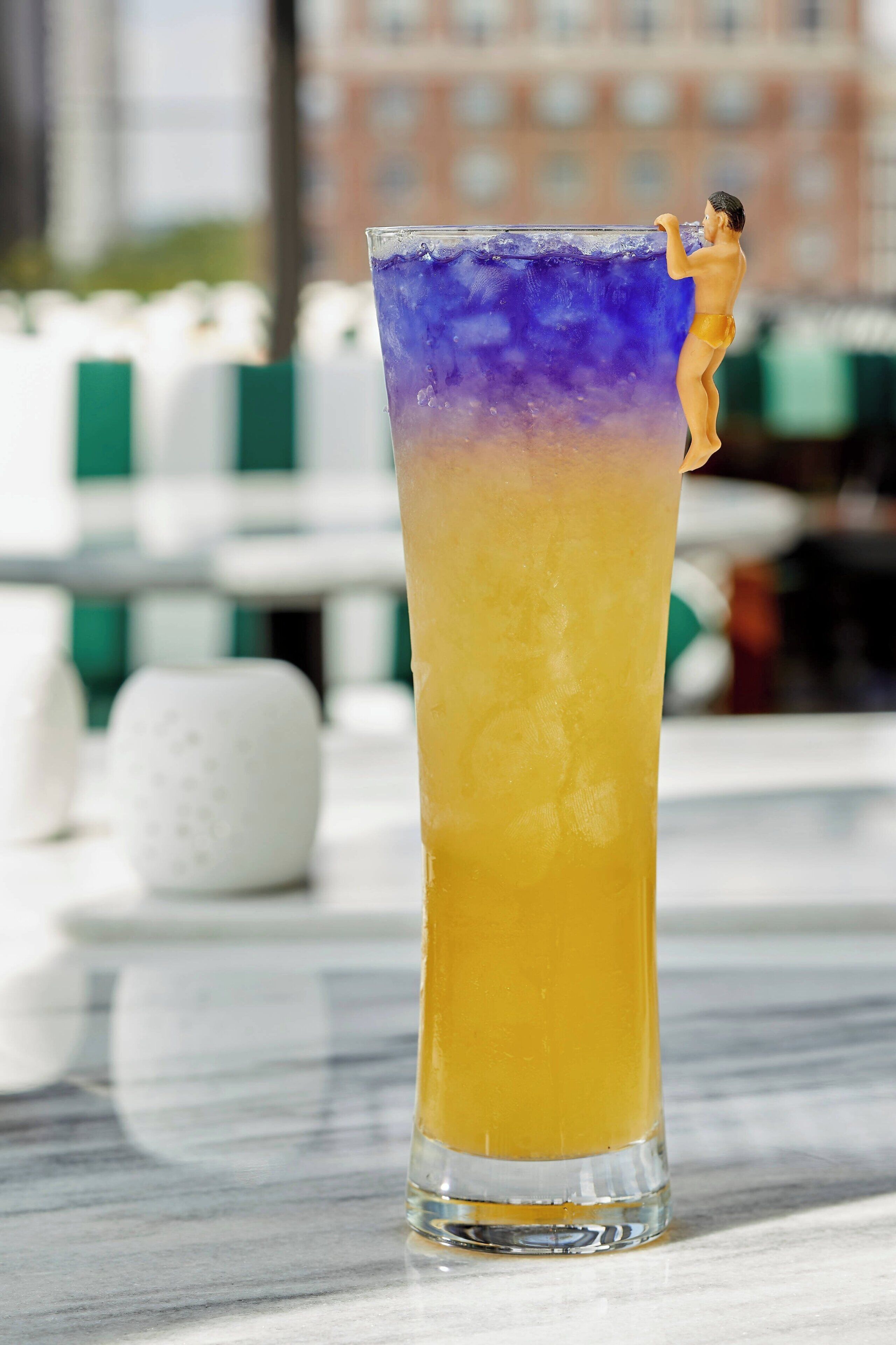 A tall glass with a gradient drink, a salt shaker, and a miniature figure on the rim.