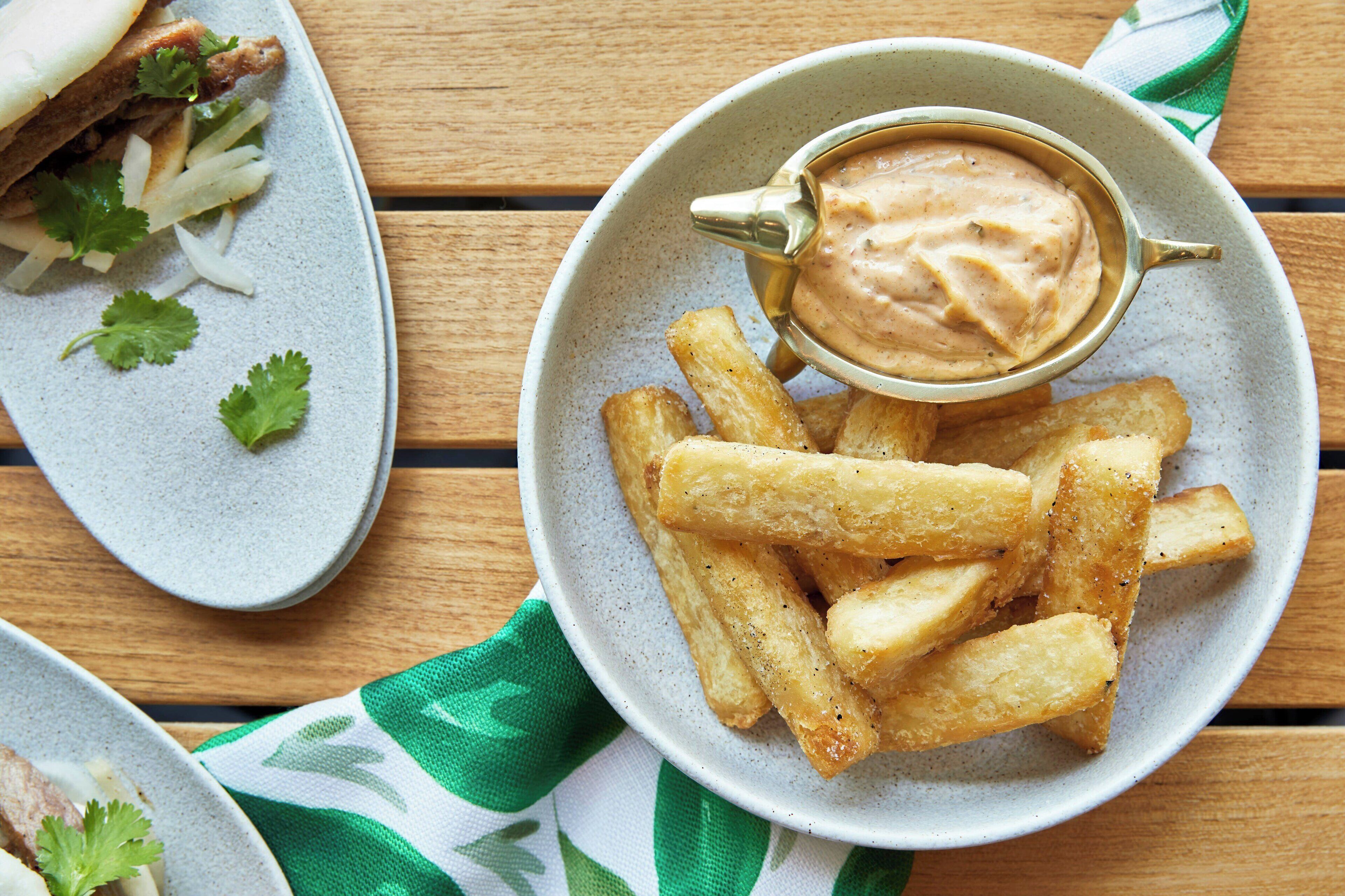 A plate of French fries with a dipping sauce and a side of meat.
