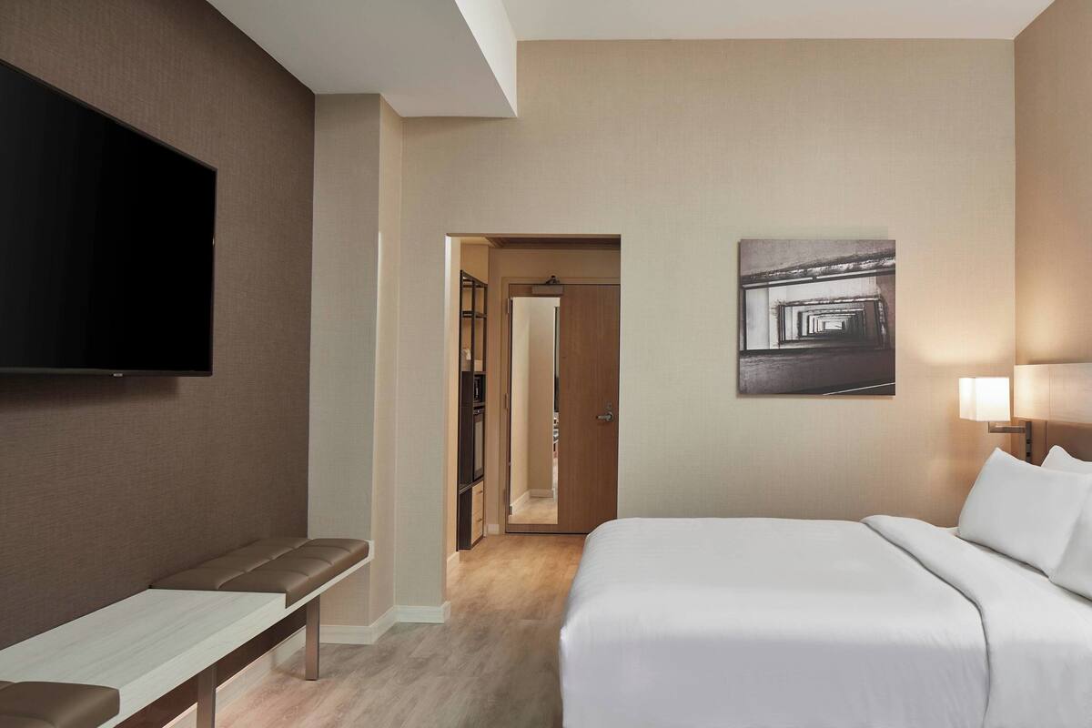 Et hotelværelse med seng, bænk, fjernsyn og et billede på væggen.