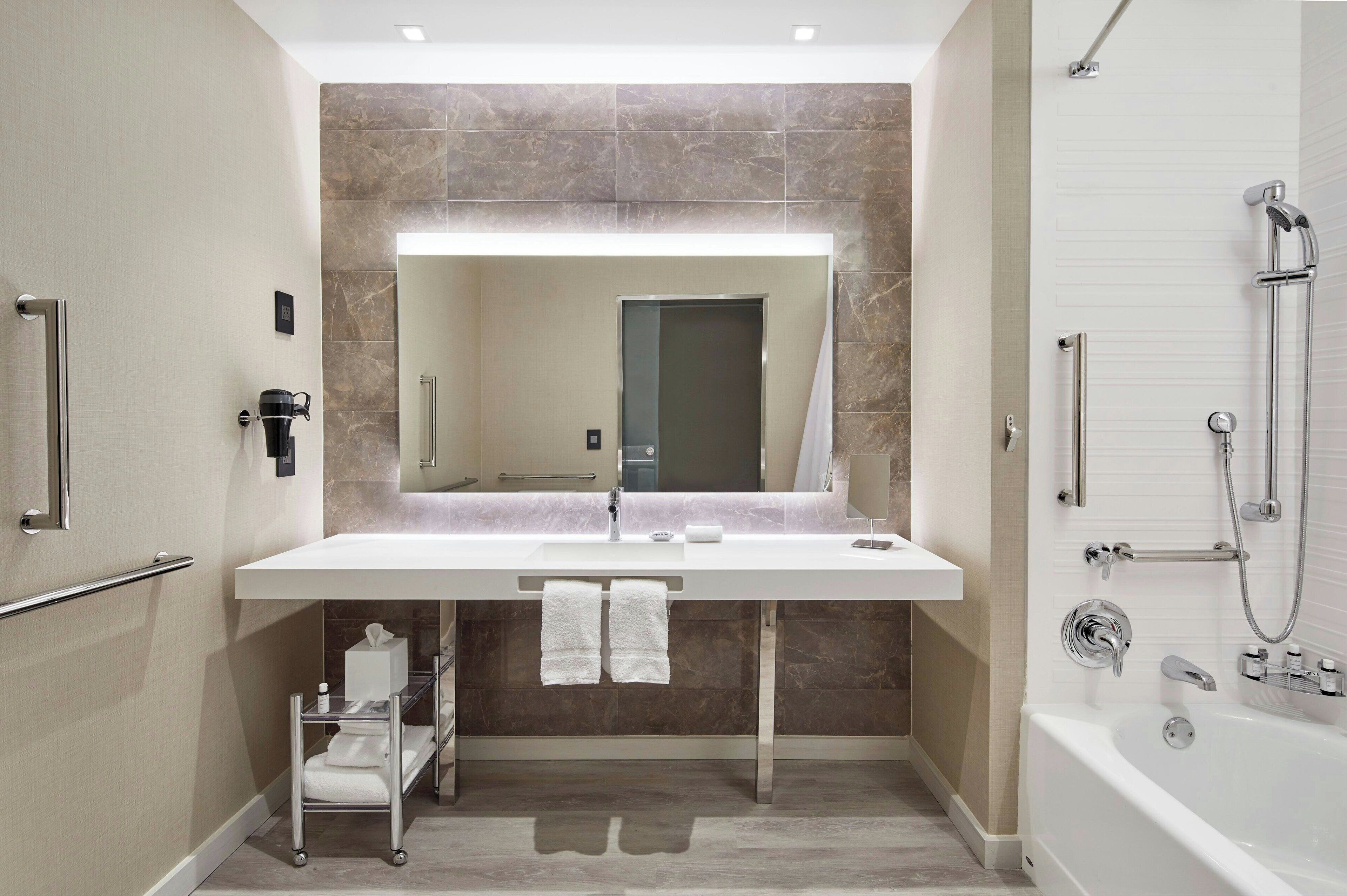 Un baño moderno con un espejo grande, un lavamanos blanco, una bañera y una zona de ducha.