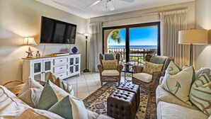 A hotel room with a balcony, wicker furniture, a flat-screen TV, and a ceiling fan.
