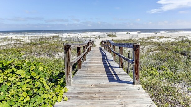 A wooden boardwalk leading to a beach with a clear sky.