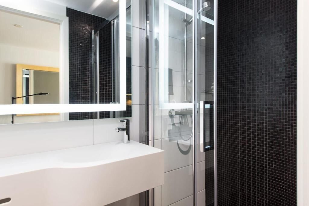 Un baño moderno con un lavabo blanco, un espejo grande y una ducha con cerramiento de vidrio.