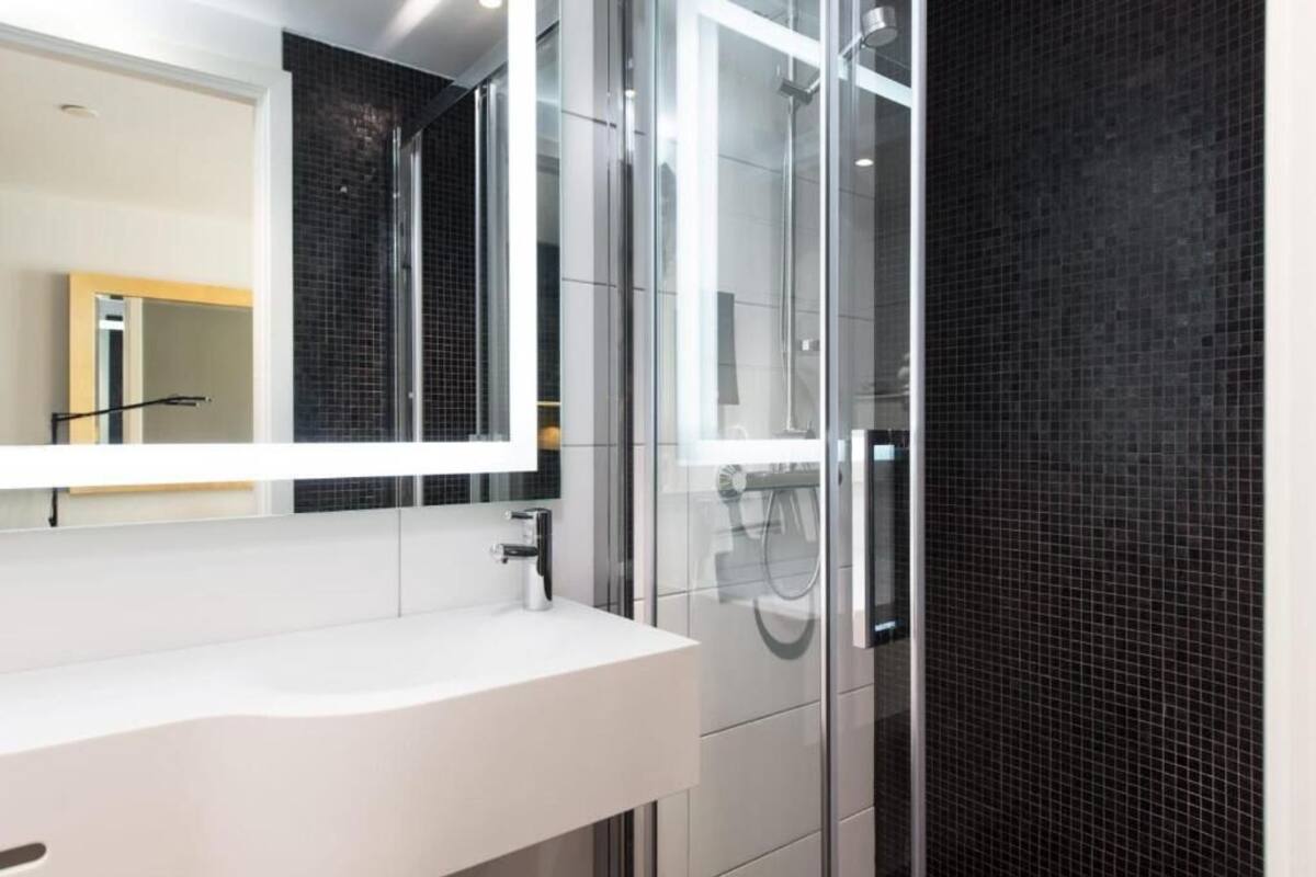 Un baño moderno con un lavabo blanco, un espejo grande y una ducha con cerramiento de vidrio.