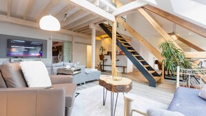 A modern loft apartment with exposed wooden beams, a staircase, a flat-screen TV, and a cozy seating area. - Holiday Apartment "Kleine Auszeit" – Your Place to Relax (Mürlenbach)
