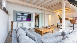 A modern living room with a large flat-screen TV, a wooden coffee table, and grey upholstered sofas. - Holiday Apartment "Kleine Auszeit" – Your Place to Relax (Mürlenbach)